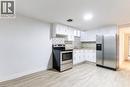 Kitchen featuring white cabinetry, stainless steel appliances, patterned tile backsplash, and light wood-finish flooring - 404 Queenston Road, Hamilton, ON 