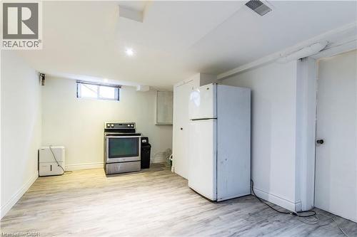 Spacious utility area featuring wood-finish flooring, a white refrigerator, and a freestanding electric range - 404 Queenston Road, Hamilton, ON 
