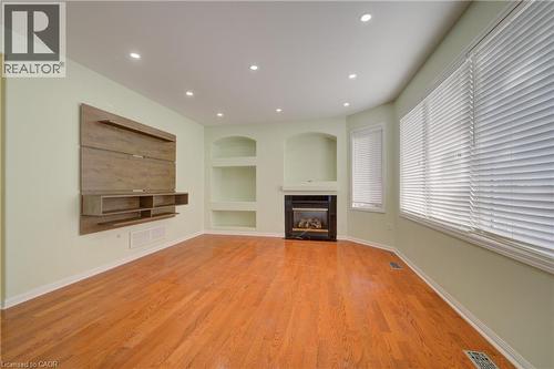 Living area featuring hardwood flooring, recessed lighting, a built-in electric fireplace with a black surround, a wood-finish media console, and multiple windows - 180 Arthur Fach Drive, Cambridge, ON 