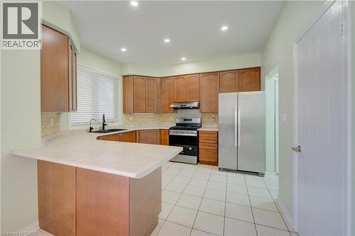 Kitchen featuring wood-finish cabinetry, light-toned countertops, a tile backsplash, and stainless steel appliances - 180 Arthur Fach Drive, Cambridge, ON 