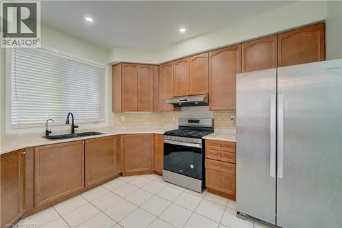 Kitchen featuring wood-finish cabinetry, stainless steel appliances, a black basin sink with a matte black faucet, light-toned countertops, and a mosaic tile backsplash - 180 Arthur Fach Drive, Cambridge, ON 