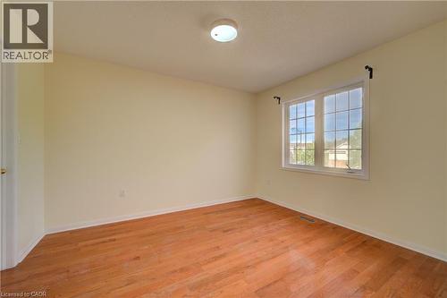 Bedroom featuring wood-finish flooring, a window with muntins, light-toned walls, white trim, and a ceiling-mounted light fixture - 180 Arthur Fach Drive, Cambridge, ON 