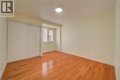 Room featuring warm wood-finish flooring, a white bi-fold closet, a double window, and light-toned walls - 180 Arthur Fach Drive, Cambridge, ON 