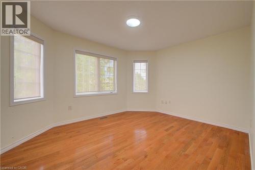 Spacious room featuring wood-finish flooring, multiple windows with roller shades, a flush-mount ceiling light, and neutral wall tones - 180 Arthur Fach Drive, Cambridge, ON 