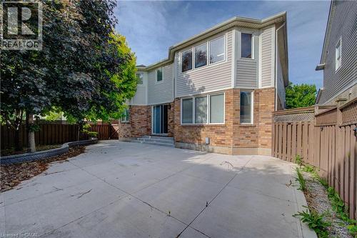 Rear exterior featuring a spacious concrete patio, brick and siding facade, multiple windows, and a sliding glass door - 180 Arthur Fach Drive, Cambridge, ON 