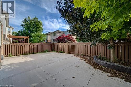 Paved patio area featuring a wooden privacy fence, mature trees, and a built-in planter with stone detailing - 180 Arthur Fach Drive, Cambridge, ON 