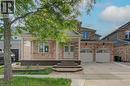 Brick-clad residence featuring a covered front porch, double entry doors, a two-car garage with carriage-style doors, a paved driveway, and mature landscaping - 180 Arthur Fach Drive, Cambridge, ON 