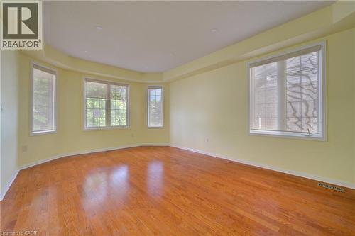 Expansive room featuring rich wood-finish flooring, a tray ceiling, and multiple windows with roller shades - 180 Arthur Fach Drive, Cambridge, ON 