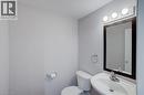 Compact powder room featuring a wall-mounted sink, a toilet, a rectangular framed mirror, and a three-bulb vanity light fixture - 53 Prosperity, Kitchener, ON 