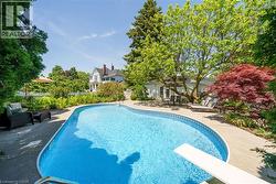Freeform swimming pool with a diving board, surrounded by concrete decking and mature trees - 