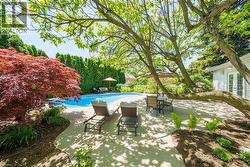 Backyard oasis featuring an in-ground swimming pool, spacious concrete patio, mature trees, and established landscaping - 