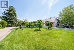 Expansive front lawn with mature trees and a white picket fence - 