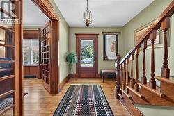 Entry foyer featuring hardwood flooring, detailed wood trim, a decorative glass-paneled front door, and a traditional turned wood staircase - 
