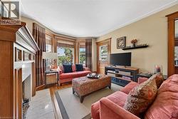 Living room featuring a prominent wood-finish mantelpiece, a bay window with window treatments, light-toned wall paint, and wood-finish flooring - 