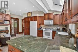 Kitchen featuring cherry-toned cabinetry, a skylight, recessed lighting, stone countertops, and a white appliance suite - 