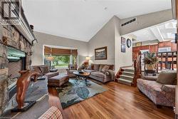 Living area featuring a stone fireplace with a raised hearth, wood-finish flooring, a vaulted ceiling, and a bay window - 
