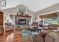 Vaulted ceiling great room featuring a stone-clad fireplace with a wood mantel, wood-finish flooring, and large windows - 