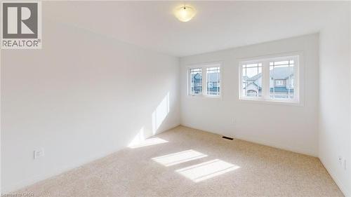 Neutral-toned carpeting paired with white walls, two windows featuring white trim and grilles, and a flush-mount ceiling light fixture - 200 Cittadella Boulevard, Hamilton, ON 