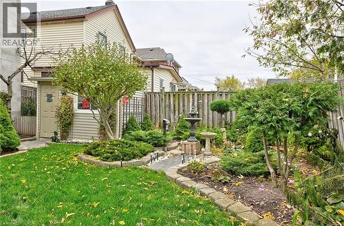 Landscaped backyard featuring a stone-lined garden path, mature shrubs, a decorative fountain, a privacy fence, and a manicured lawn - 1476 Barton Street E Unit# 2, Hamilton, ON 