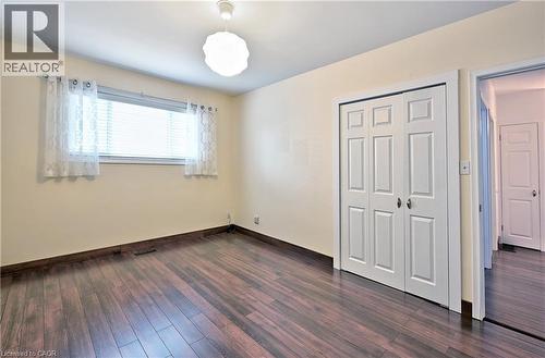 Room featuring rich wood-finish flooring, a contemporary ceiling light fixture, a window with horizontal blinds, and a paneled bifold closet door - 1476 Barton Street E Unit# 2, Hamilton, ON 