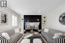 Living room featuring an ornate fireplace with a black accent wall, symmetrical built-in shelving, crown molding, recessed lighting, and wall paneling - 