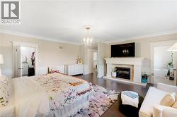 Spacious room featuring dark wood-finish flooring, a traditional fireplace with a stone mantel, crown molding, and wainscoting - 