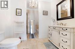 Bathroom featuring a distressed white vanity with dark hardware, a rectangular mirror, and a crystal chandelier - 