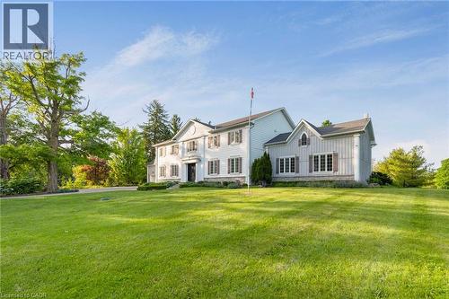 Expansive green lawn with mature trees framing a traditional-style property featuring white siding and dark shutters - 6195 Milburough Line, Burlington, ON - Outdoor