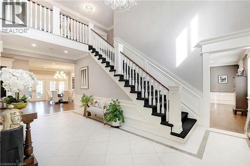 Grand entry foyer featuring white tile flooring with a grey border, a prominent staircase with white balusters and dark treads, a second-story landing with matching balusters, and crown molding accent - 6195 Milburough Line, Burlington, ON - Indoor Photo Showing Other Room