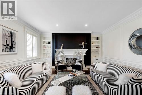 Living room featuring an ornate fireplace with a black accent wall, symmetrical built-in shelving, crown molding, recessed lighting, and wall paneling - 6195 Milburough Line, Burlington, ON - Indoor