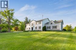 Expansive green lawn with mature trees framing a traditional-style property featuring white siding and dark shutters - 