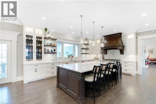 Gourmet kitchen featuring a large central island with seating, white perimeter cabinetry, a wood-finish range hood, and wood-finish flooring - 6195 Milburough Line, Burlington, ON - Indoor Photo Showing Kitchen With Upgraded Kitchen