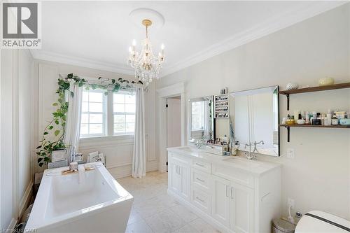 Bright bathroom featuring a freestanding tub, double vanity with integrated sinks, and a crystal chandelier - 6195 Milburough Line, Burlington, ON - Indoor Photo Showing Bathroom
