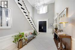 Two-story foyer featuring a grand staircase with dark treads and white risers, double entry doors, a large chandelier, and wainscoting - 