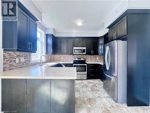 Kitchen featuring dark wood cabinetry, light-toned countertops, and a mosaic tile backsplash - 154 Rosemount Drive, Kitchener, ON 