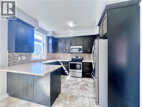 Spacious kitchen featuring dark wood cabinetry, light-toned countertops, stainless steel appliances, a mosaic tile backsplash, and ceramic tile flooring - 154 Rosemount Drive, Kitchener, ON 