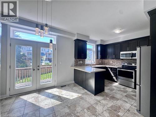 Kitchen featuring dark wood cabinetry, stainless steel appliances, a white stone countertop, a mosaic tile backsplash, and a breakfast bar - 154 Rosemount Drive, Kitchener, ON 