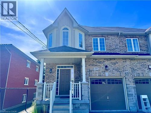Stone and siding facade featuring a prominent gabled entry, bay window with arched transom, covered front porch, and an integrated single-car garage with arched window accents - 154 Rosemount Drive, Kitchener, ON 