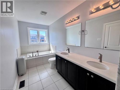 Full bathroom featuring a dual sink vanity with dark cabinetry and light countertops, two wall-mounted vanity lights, and a built-in tub with a tiled surround - 154 Rosemount Drive, Kitchener, ON 