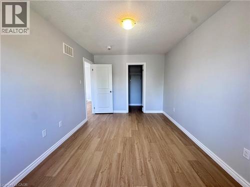 Spacious room featuring wood-finish flooring, light grey painted walls, white baseboards, and a ceiling-mounted light fixture - 154 Rosemount Drive, Kitchener, ON 