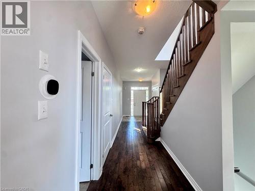 Hallway featuring wood-finish flooring, light grey walls, and a prominent wood staircase with matching railing - 154 Rosemount Drive, Kitchener, ON 
