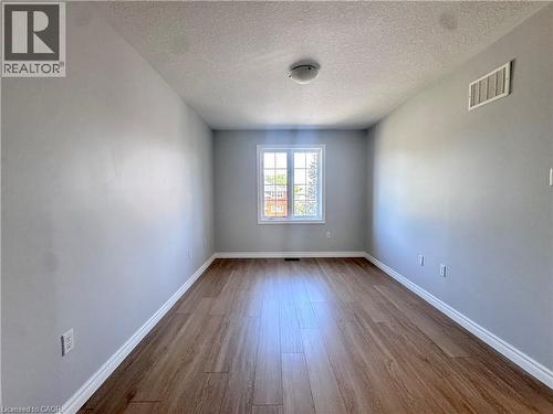 Spacious room featuring wood-finish flooring, light gray walls, a central window with white trim, and a ceiling-mounted light fixture - 154 Rosemount Drive, Kitchener, ON 