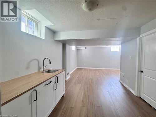 Lower level featuring wood-finish flooring and a functional wet bar with a stainless steel sink, pull-down faucet, white cabinetry, and matte black hardware - 154 Rosemount Drive, Kitchener, ON 