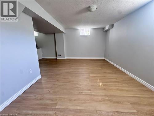 Spacious room featuring wood-finish flooring, light gray walls, white baseboards, and a recessed window - 154 Rosemount Drive, Kitchener, ON 