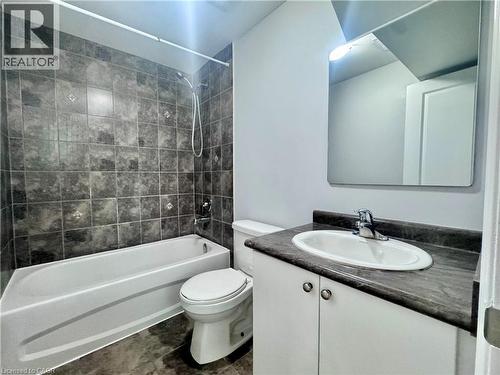Bathroom featuring a full tub with shower, dark tile surround, single vanity with integrated sink, and wall-mounted mirror - 154 Rosemount Drive, Kitchener, ON 