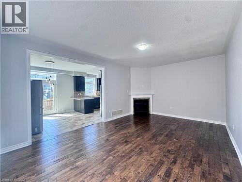 Spacious living area featuring rich wood-finish flooring, a built-in fireplace with a white mantel, and light gray wall tones - 154 Rosemount Drive, Kitchener, ON 