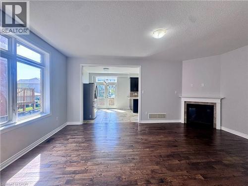 Spacious living area featuring wood-finish flooring, a decorative fireplace with a white mantel, and ample natural light from a large window - 154 Rosemount Drive, Kitchener, ON 