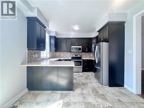Kitchen featuring dark wood-finish cabinetry, light-toned countertops, and a mosaic tile backsplash - 154 Rosemount Drive, Kitchener, ON 