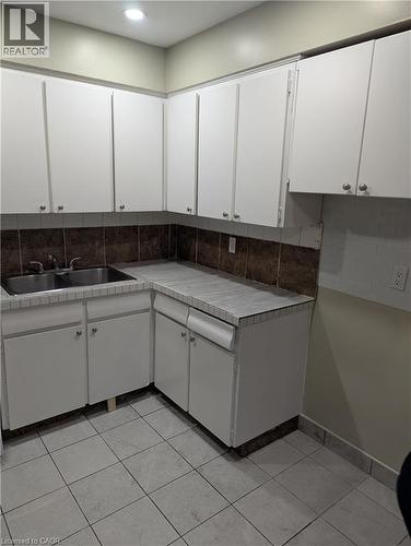 Kitchen featuring white cabinetry, tile flooring, a double basin stainless steel sink, and a tiled backsplash - 949 E Main Street E, Hamilton, ON 