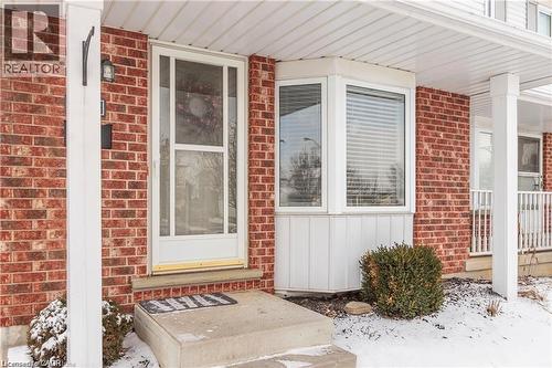 Brick exterior featuring a white storm door, concrete entry pad, and a prominent bay window with horizontal blinds - 209 Auburn Drive Unit# A, Waterloo, ON 